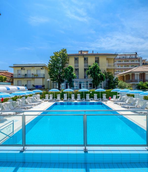 Piscina all'aperto con lettini e ombrelloni, cielo sereno.