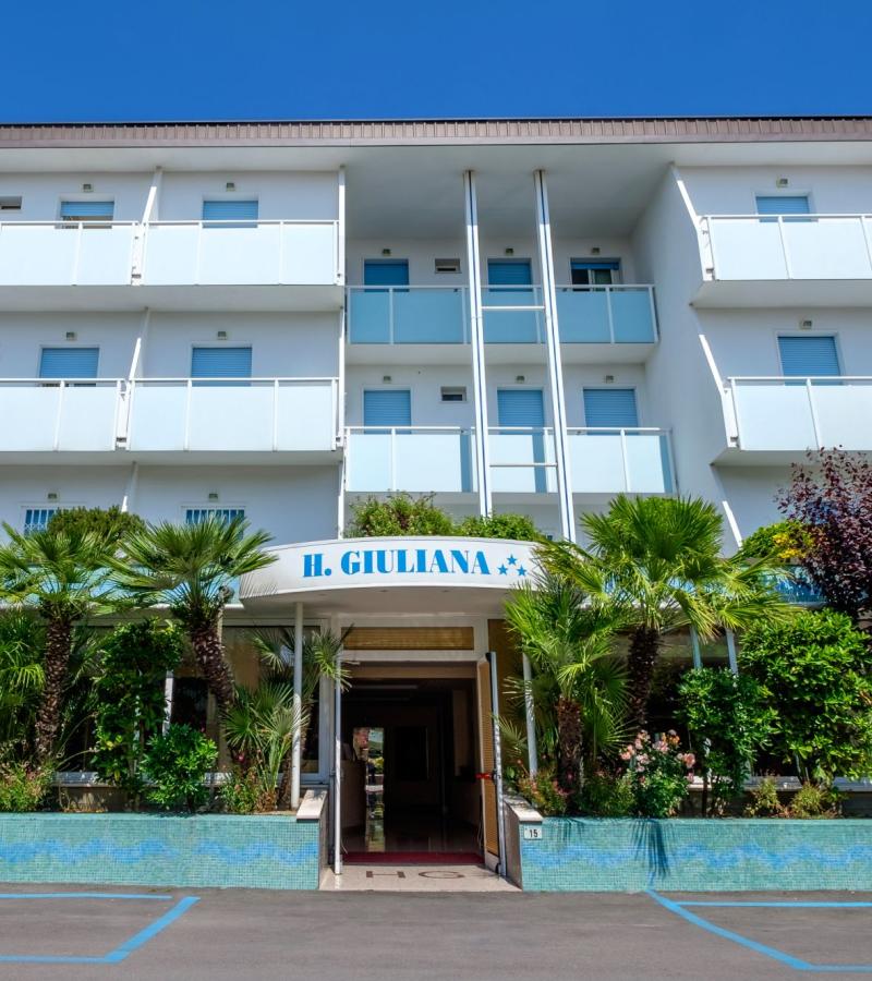 Hotel moderno con balconi, giardino e parcheggio, cielo blu sopra.