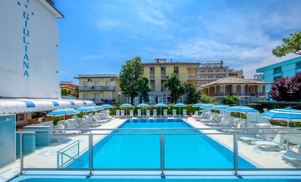 Piscina all'aperto con lettini e ombrelloni, cielo sereno.