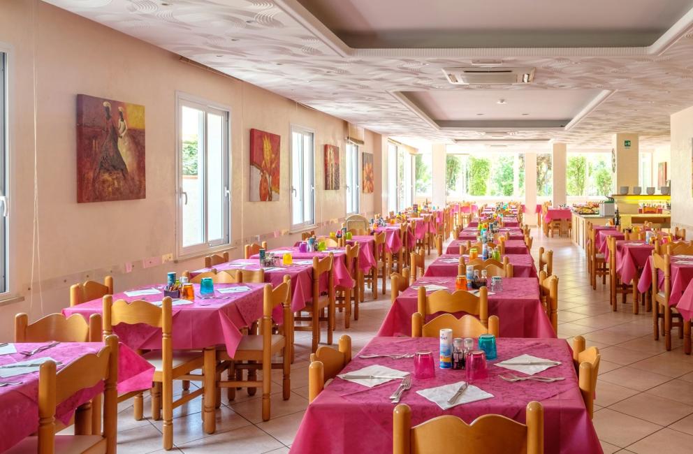 Ristorante con tavoli apparecchiati e tovaglie rosa, decorato con quadri floreali.