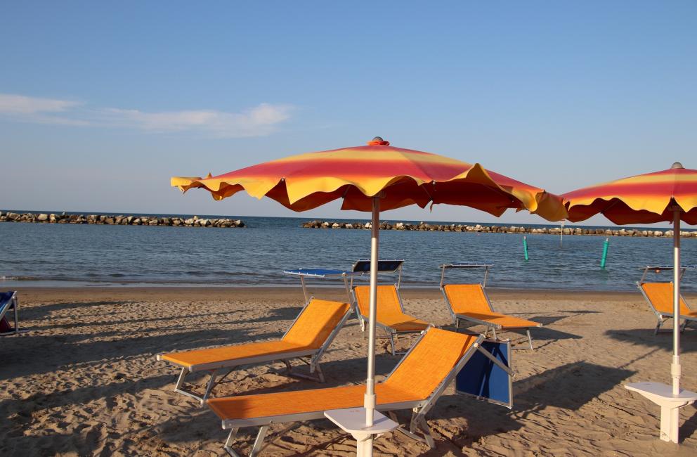 Spiaggia con ombrelloni arancioni e lettini, mare calmo sullo sfondo.