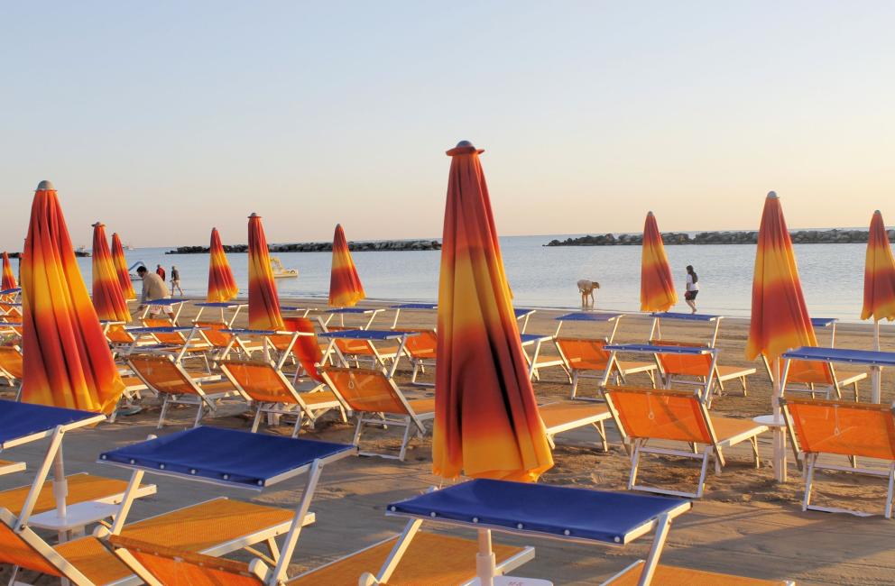 Spiaggia al tramonto con ombrelloni arancioni e lettini vuoti.